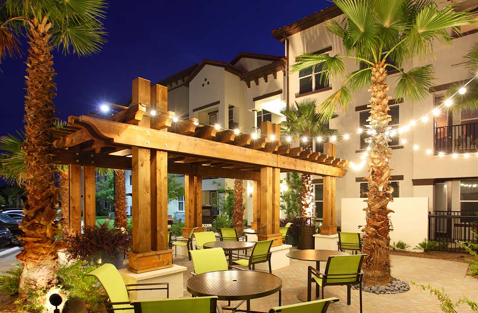 jefferson westshore outdoor living area at night with tables, chairs, pergola and view of apartment building with balconies in the background - jefferson apartment group