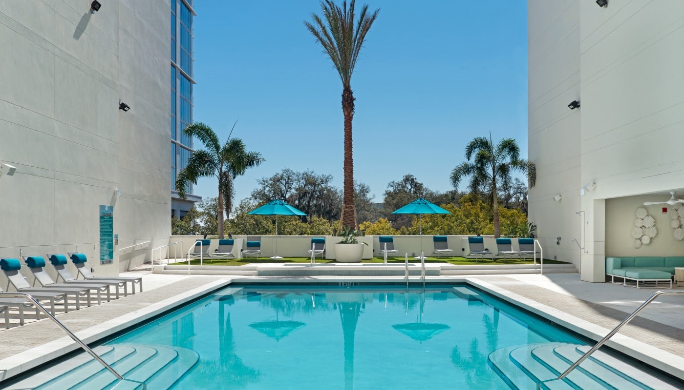 420 east resort style pool with chaise lounge chairs, palm trees, social seating and view of wooded area in the background - jefferson apartment group