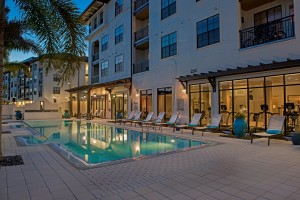 azul resort style pool at night with chaise lounge chairs, view of fitness center and apartment building in the background - jefferson apartment group