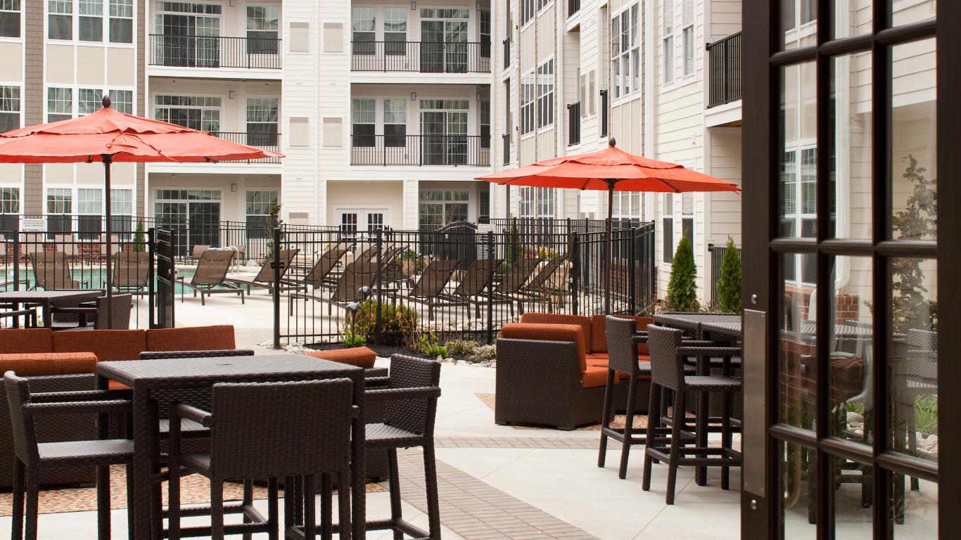 jefferson pointe at west chster outdoor lounge with tables, chairs, social seating and view of pool and apartment building in the background - jefferson apartment group