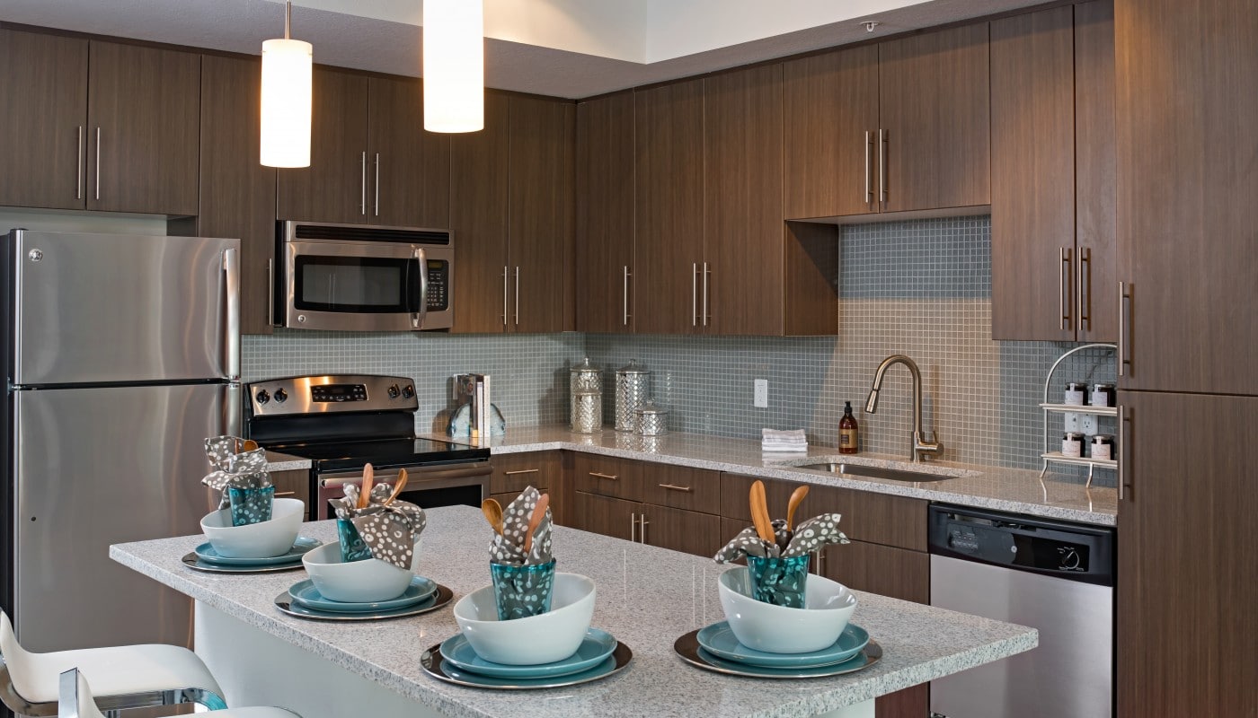kitchen with granite island, dark wood cabinetry, modern lighting, stainless steel appliances and a tile backsplash - jefferson apartment group