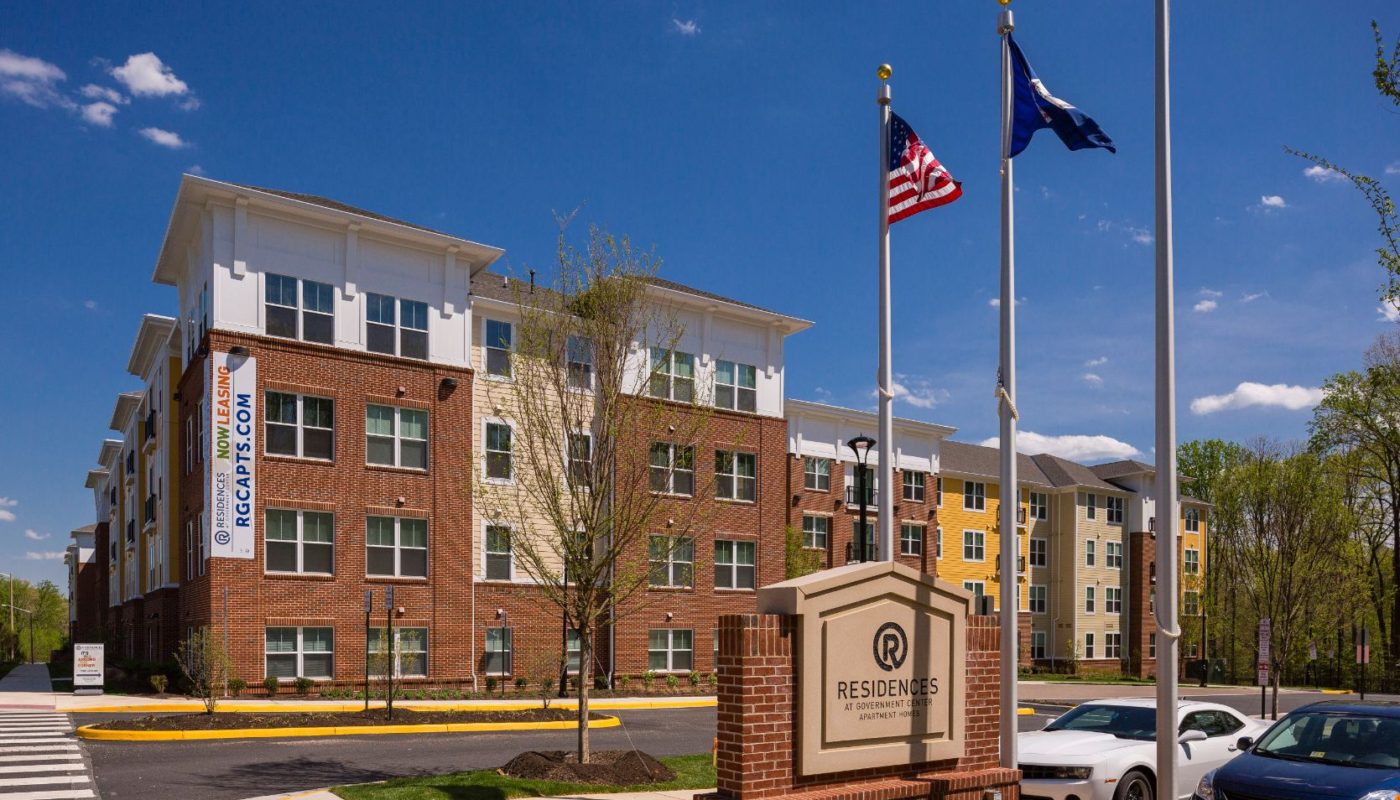 exterior of 4 story apartment building called residences at government center with monument sign and US and VA flags in fairfax va
