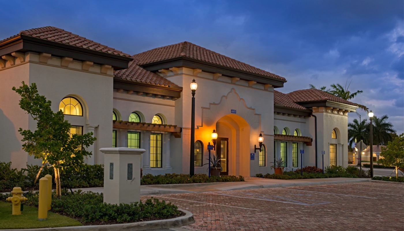 lighthouse point resident lounge exterior at night with trees, landscaping, spanish tile roof and parking area - jefferson apartment group