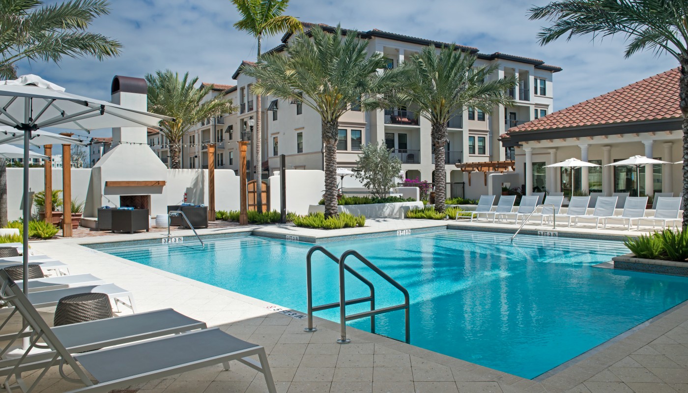light house point resort style pool with chaise lounge chairs, umbrellas, palm frees and fireplace - jefferson apartment group