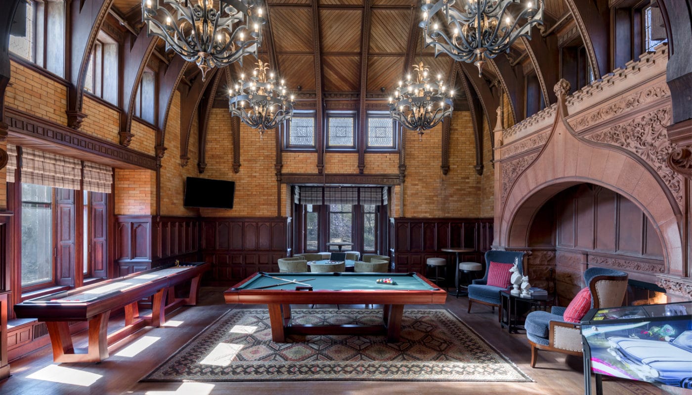 maybrook mansion game room with shuffleboard, billiards, pinball machine, fireplace, chandeliers and intricate details on walls, ceiling and fireplace surround - jefferson apartment group