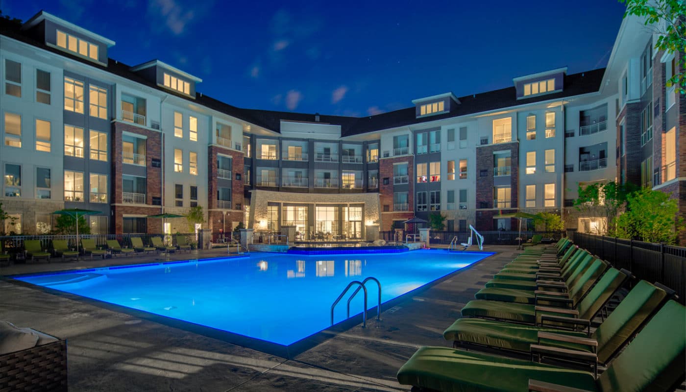 maybrook resort style pool with chaise lounge chairs, umbrellas, greenery, and view of apartment building in the background - jefferson apartment group