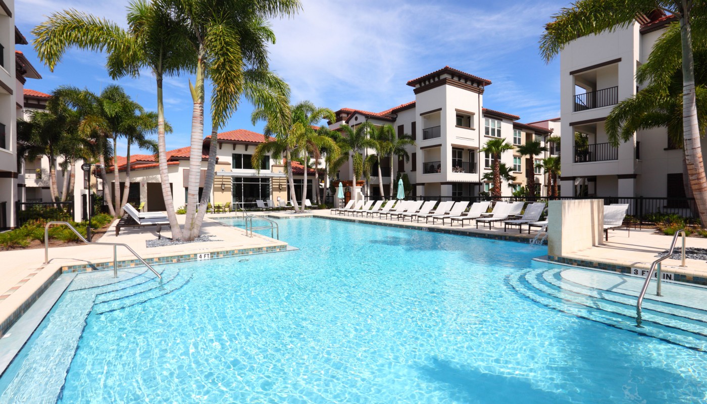 westshore resort style pool with chaise lounge chairs palm trees, and view of apartment building with balconies in the background - jefferson apartment group