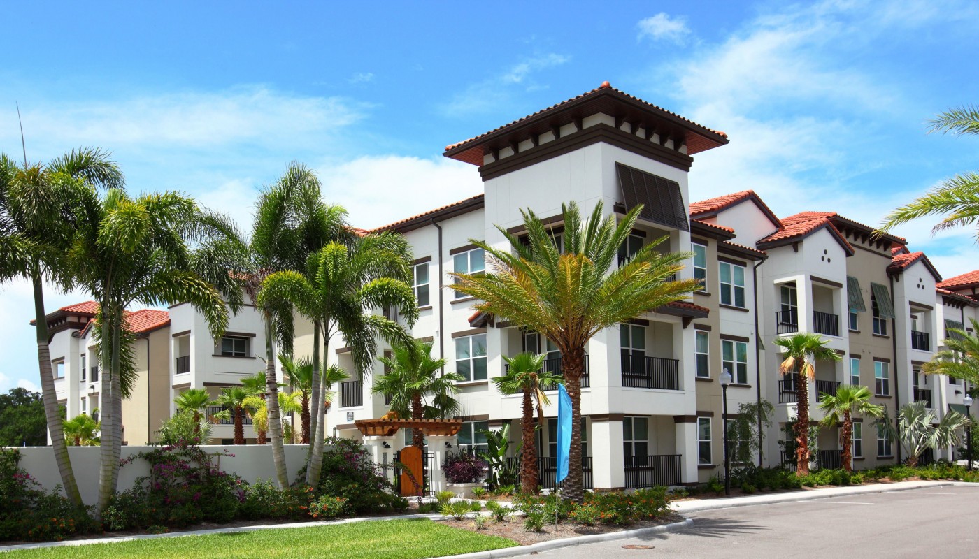 westshore exterior showing a three story building with balconies, palm trees and gated entrance - jefferson apartment group