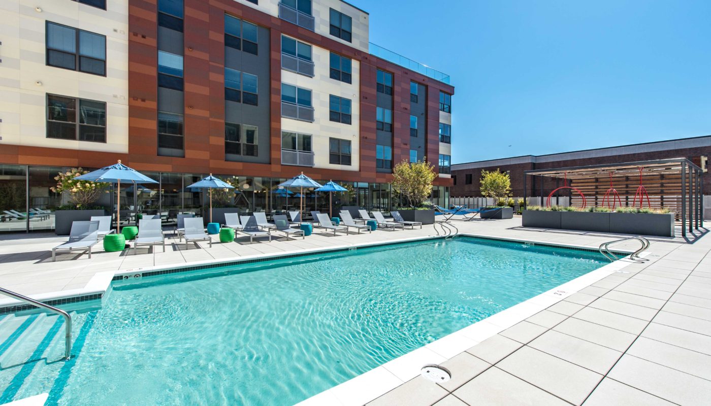 j malden center resort style pool with chaise lounge chairs, umbrellas, cocktail tables, and view of apartments and swing chairs in the background - jefferson apartment group