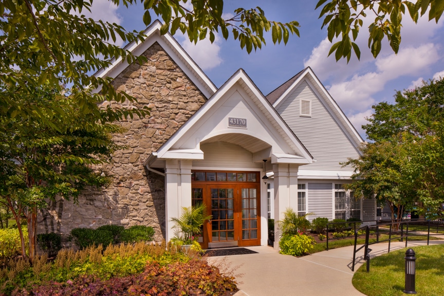 arbors at broadlands clubhouse with lush landscaping, trees and blue sky - jefferson apartment group