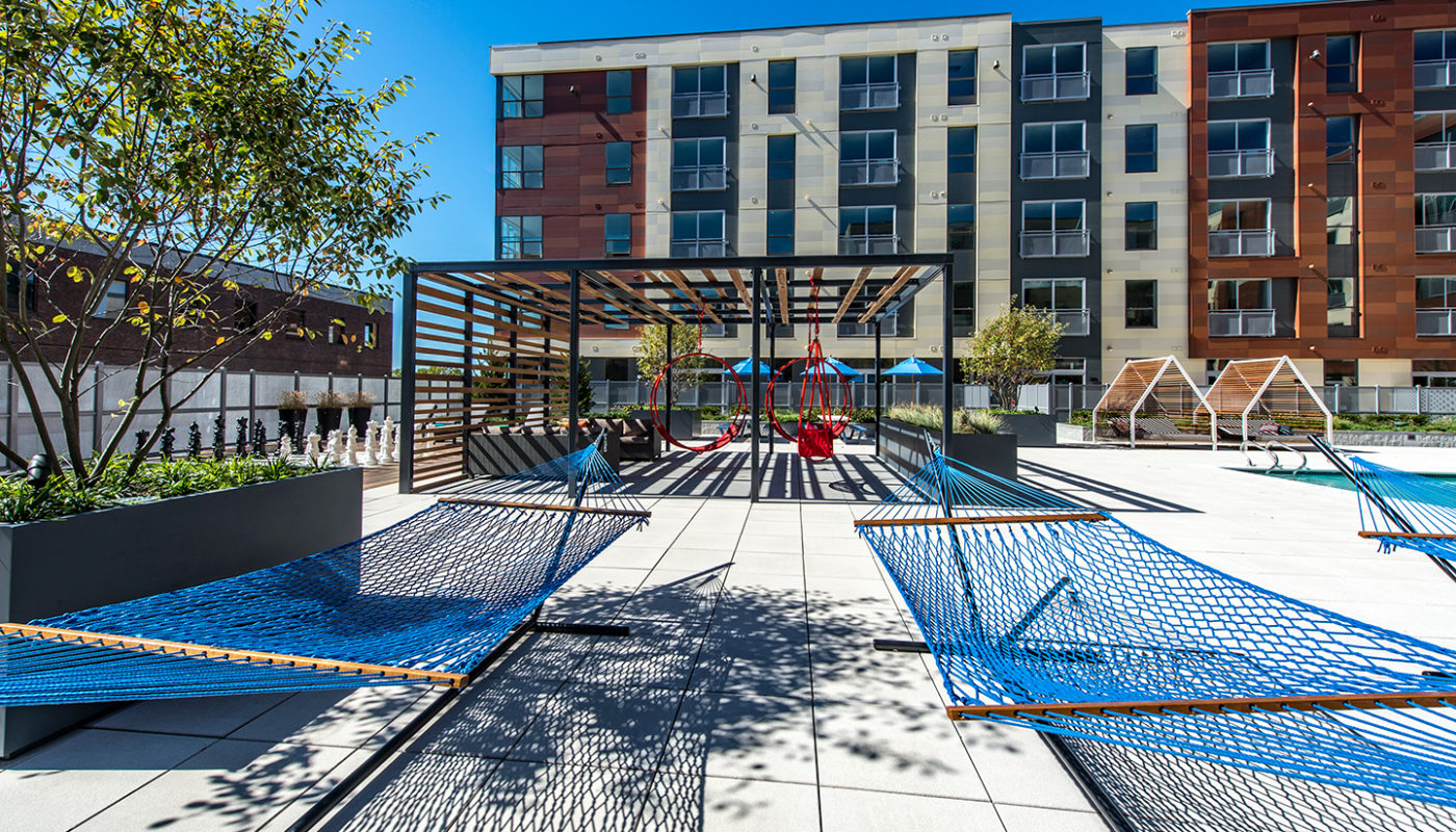 j malden center hammocks next to resort style pool and red swing chairs with apartment building in the background - jefferson apartment group