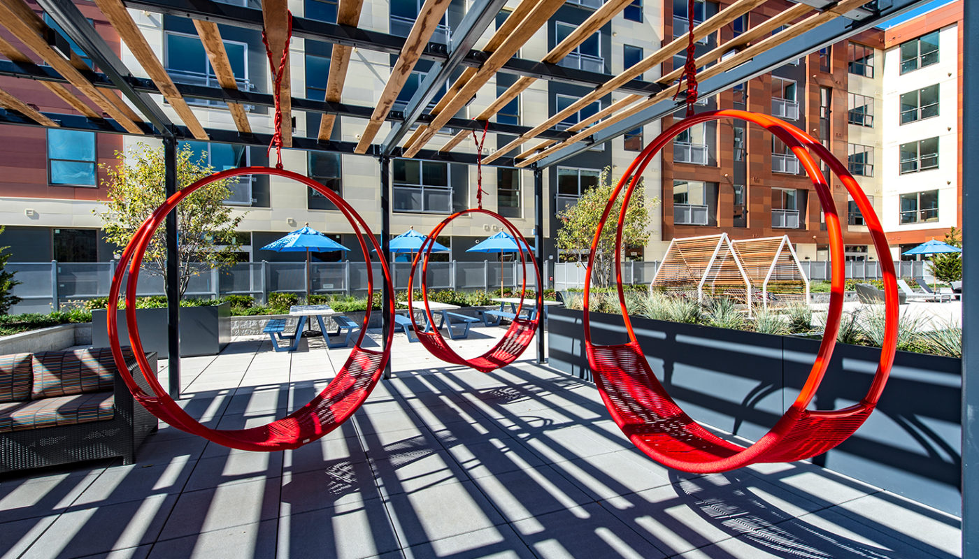 j malden center red swing chairs under pergola with view of picnic tables, chairs and apartment building in the background - jefferson apartment group