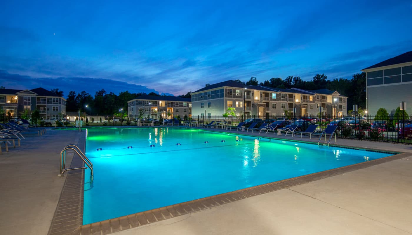 emblem at christiana resort style pool at night with chaise lounge chairs, and view of apartment buildings in the background - jefferson apartment group