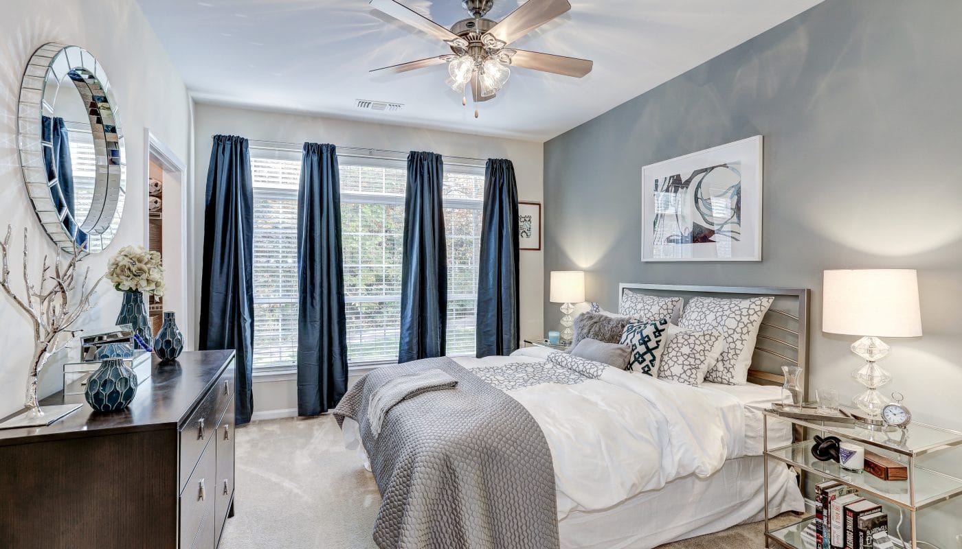 arbors at broadlands bedroom with bed, dresser, night stand, large windows, ceiling fan and modern artwork - jefferson apartment group