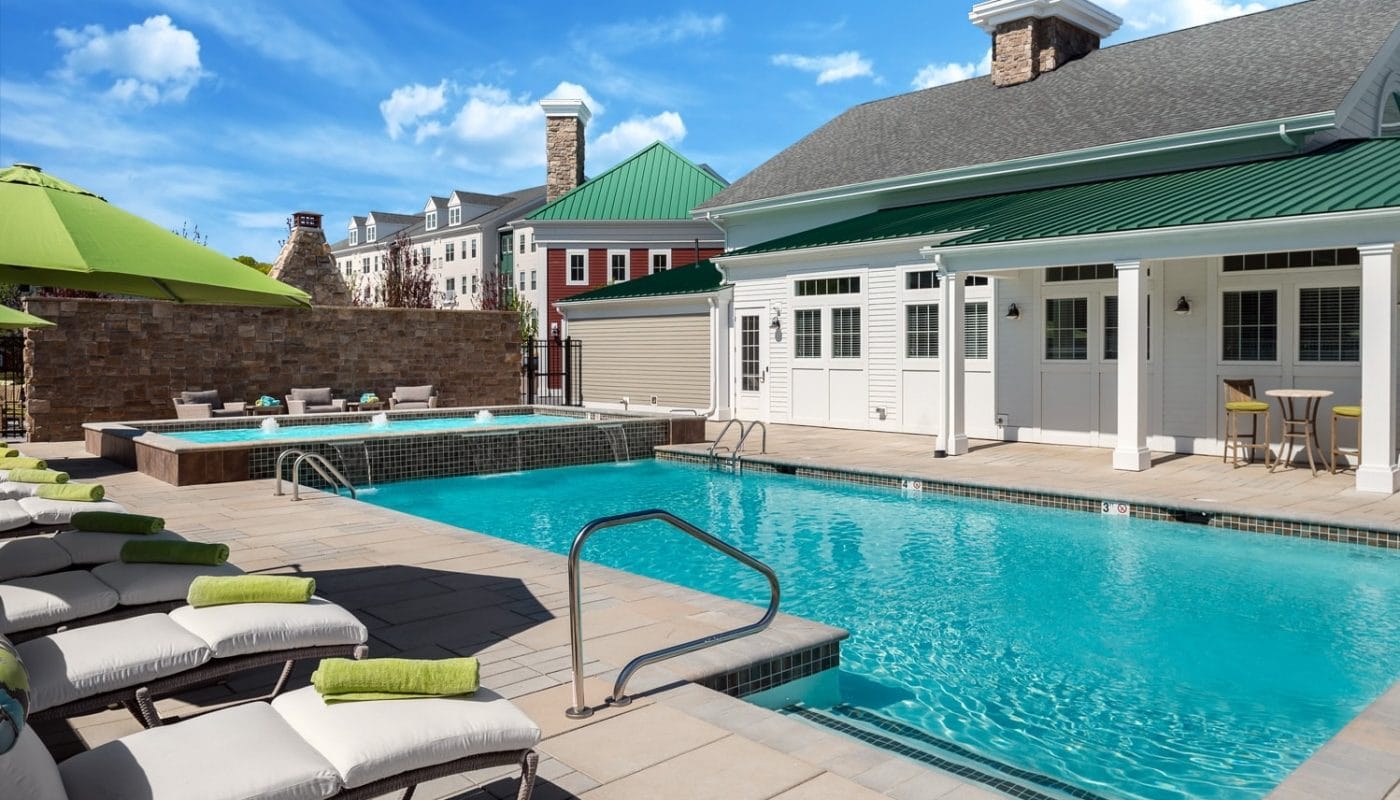 one upland resort style pool with water features, chaise lounge chairs, umbrellas and view of club house - jefferson apartment group