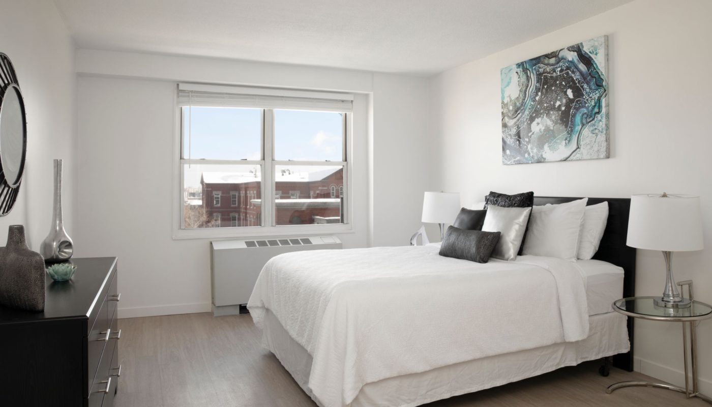 Bedroom with bed, dresser, mirror, night stand, modern artwork and large window in boston ma