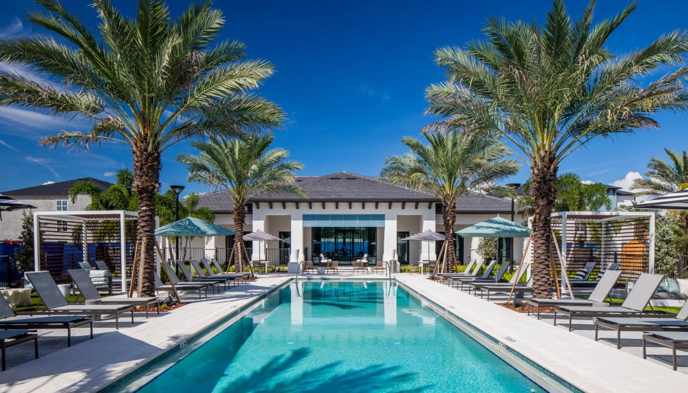 swimming pool with palm trees, lounge chairs, umbrellas and view of outdoor lounge at jefferson lake howell luxury apartments in Casselberry