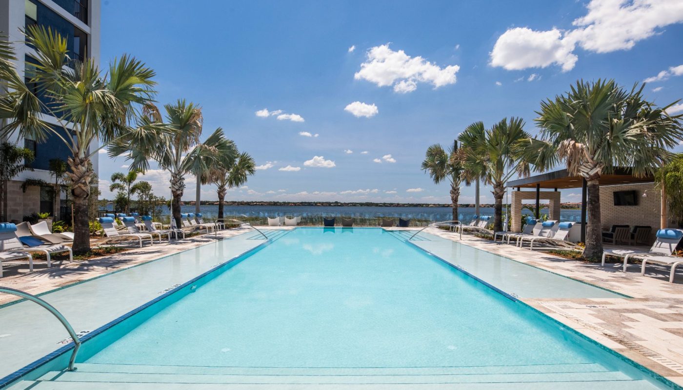 pool with chaise lounge chairs, palm trees and view of big sand lake at Orlando luxury apartments