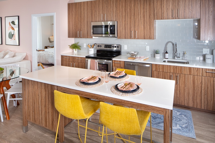 kitchen with moveable island, stainless steel appliances, wood cabinetry, quartz counters, tile backsplash and views of the bedroom and living area at scout on the circle luxury fairfax apartments