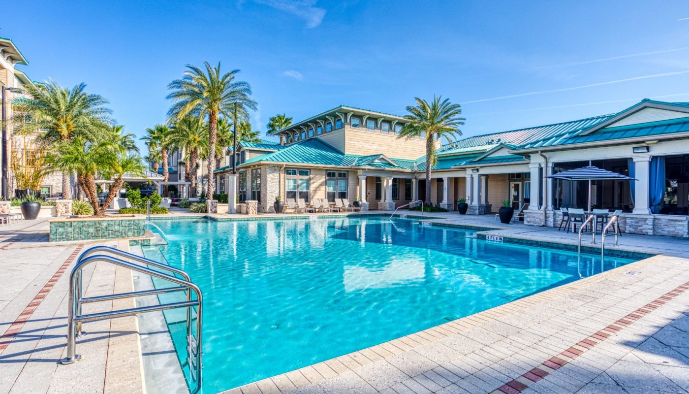 swimming pool with lounge chairs, social seating, umbrellas and a view of the club house at sea isle luxury orlando apartments