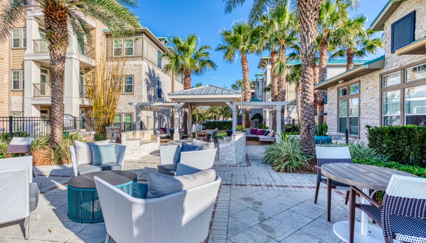 outdoor courtyard with palm trees, social seating, pergola and view of the apartment balconies at sea isle luxury orlando apartments
